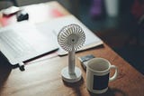 A desk with some papers, a mug, and a small fan