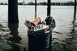 An overflowing garbage can surrounded by water in a flooded landscape