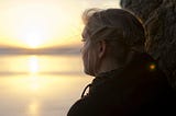 Black and white picture of a girl staring out into the sunset as you slowly dips below the ocean. The image was chosen by Spiritual Lifestyle writer Christine McDonald to showcase being an observer of life, self and spirit.