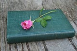Green, hardback book with a pink rose lying on top