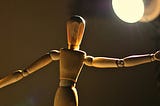 A wooden puppet in a spotlight with arms stretched out.