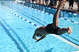 A guy diving into a competitive swimming pool during a swim race. In conjunction with my article about coaching a Men’s Division III College swim team.