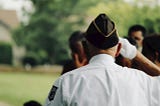 Mickey Markoff Air Sea Exec 2024 — photo of man in military uniform with POW patch on arm saluting crowd. Posted on 2024 Mickey Markoff article on net worth of paying tribute to our nation’s heroes.