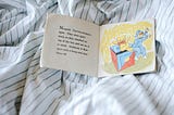 A children’s book open on a striped sheets.