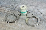 Picture of a wad of money encircled by a pair of handcuffes via Alt text on Medium