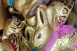 Close-up of a jumble of Lindt chocolate bunnies. They are covered in gold foil with rabbit eyes, ears, and whiskers printed in brown. Each bunny wears a coloured ribbon as a collar with a little bell on it