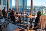 Four people working on their laptops at a long desk that is facing a window.