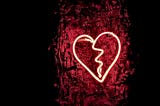 It’s a neon broken heart, looking like a valentine with a zig-zag crack down the middle, posted on a wooden log.