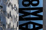 The exterior of The MOMA Museum. A sign running down the side of the building that says “MOMA”.