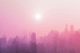 Hazy image of a city skyline with a blazing hot sun in the sky.