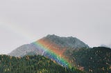 A rainbow shining over rolling hills dotted with pine trees