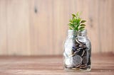 A mason jar filled with coins and a growing plant.
