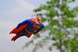 An action figure of Superman flies through the air in front of a green tree