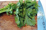 A bunch of broccoli rabe on a cutting board with a chef’s knife