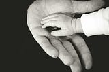 Black and white photo of a child’s hand resting in the palm of an adult hand. Photo used by author Christine McDonald to depict building confidence by placing trust in something bigger. The child’s hand resembling mankind, the adult’s hand resembling God.