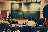 Students sit in a class with algebra on the chalkboard