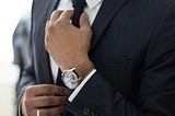 A man in a suit, wearing a nice watch, straightening his tie.