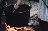 A woman stirring ingredients into a cauldron over a fire