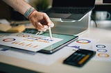 Hand pointing to chart on paper with a calculator next to it