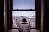 A man in a grey hoodie looking from his window in the distance on New York city in America