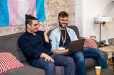 Two Makers Learners sitting together on a sofa, pair programming and smiling