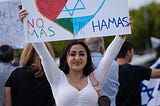 A woman holding up a sign with Palestinian and Israeli flags combined in a heart stating: “no mas Hamas”