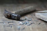 A builder’s hammer and nails laid down on a table. Because writing is building.
