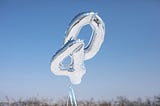 two silver mylar balloons, one in the shape of the number four, the other a zero, floating with the sky in the background