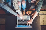 Three people sitting in front of the laptop and pointing fingers at the screen showing things to each other