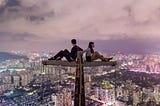 A man and a woman sitting in opposite directions on top of a very high structure.