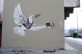 A Bansky graffiti showing a white dove carrying an olive branch being targeted with by a sniper