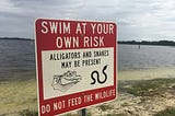 Sign that warns people to avoid swimming in the water as alligators and snakes make their home there.