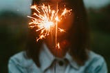 A woman with dark hair holds a sparkler in front of her face