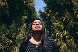 A Black woman in nature with her eyes closed and a peaceful look on her face.