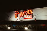 An orange neon sign reading “The Taco Stand.”