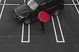 A black SUV in an empty parking lot with a person holding a red umbrella next to it.