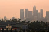 A view of downtown L.A over the shoulder of Dodger Stadium, on a hazy with a peachy orange sky.