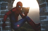 Picture of someone dressed up as Spiderman, sitting in a brick archway as he reads a book with apparent interest.