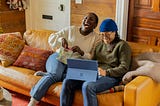 2 women sitting on a sofa in front of a laptop laughing