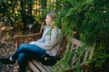 woman sitting on a bench behind an evergreen tree