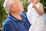 A grandpa holds his granddaughter in his arms.