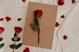 This is a photo of roses on a white background and one rose is on a brown envelope.