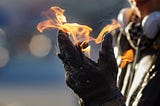 A person’s gloved hand with a flame on the palm and fingertips