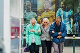 3 elderly people walking in front of a poster of 3 young famous soccer players