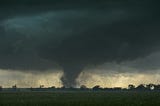 Tornado in distance along a treeline with ominous clouds overhead