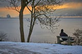 A person contemplating life sitting by a large lake