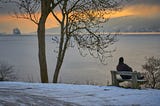 A person contemplating life sitting by a large lake