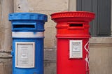 Blue post, red post side by side near a wall for people sending letters.