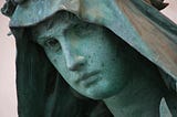 A stone statue of a troubled face under a hood.