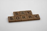 Wooden scrabble tiles spelling “Say Sorry”